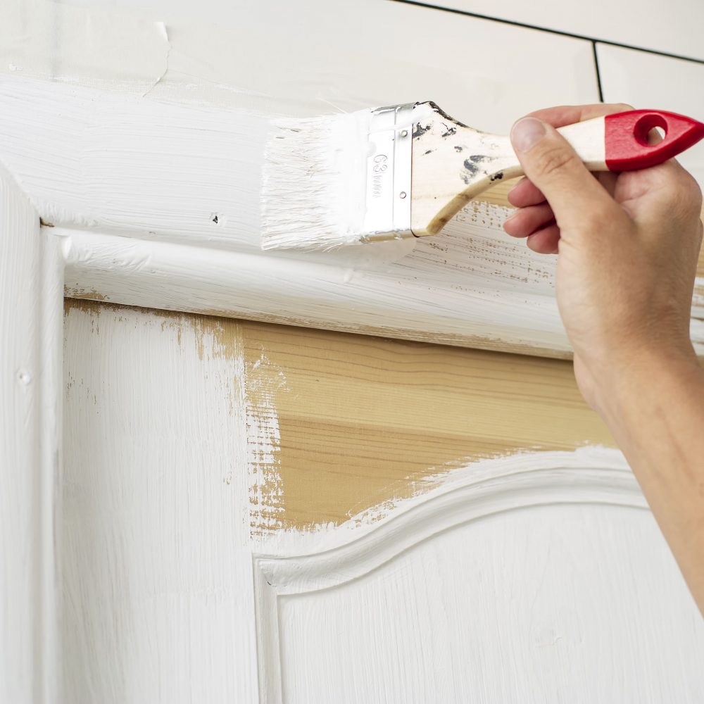 Persona pintando una puerta de madera con pintura blanca