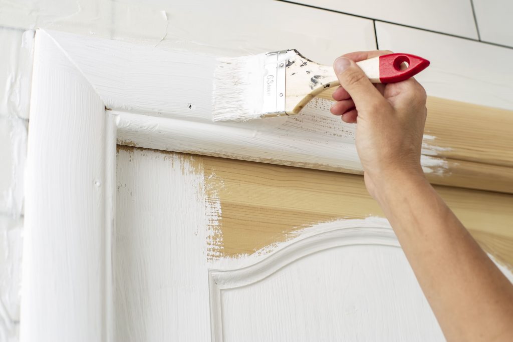 Persona pintando una puerta de madera con pintura blanca